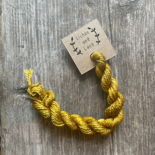 A skein of Amber yellow embroidery yarn labelled 'Lichen and Lace'.