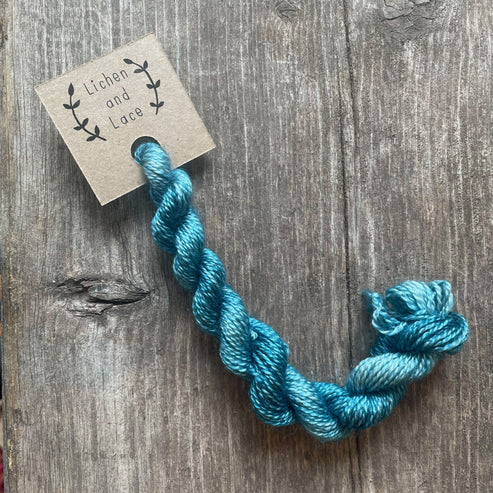 A skein of Blue Lagoon blue embroidery yarn labelled 'Lichen and Lace'.