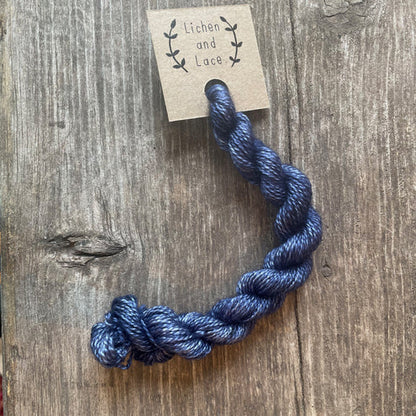 A skein of Calm Waters dark blue embroidery yarn labelled 'Lichen and Lace'.