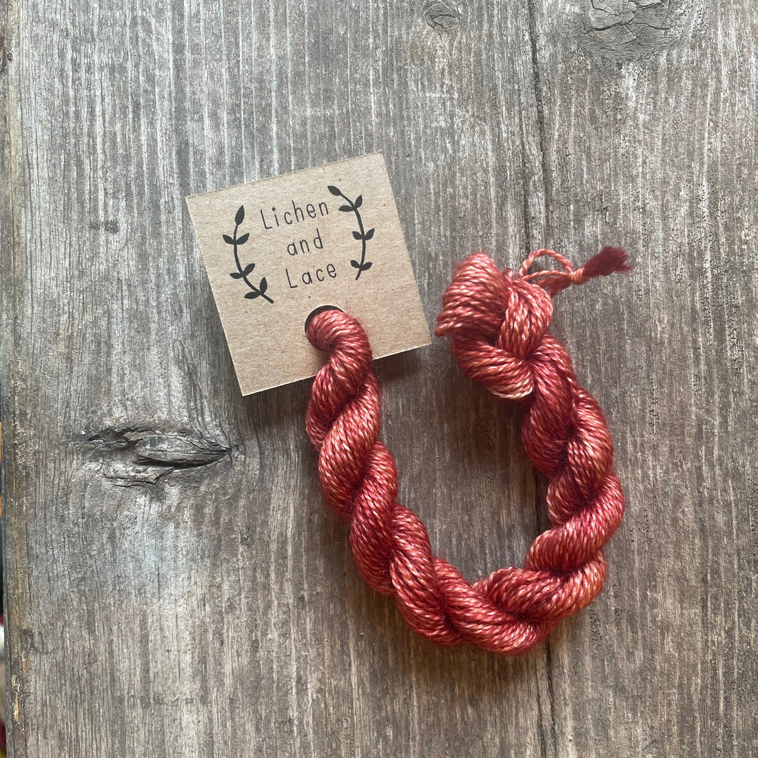 A skein of Coral pink embroidery yarn labelled 'Lichen and Lace'.