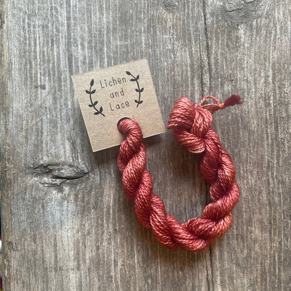A skein of Coral pink embroidery yarn labelled 'Lichen and Lace'.