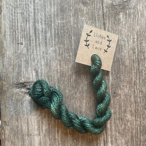 A skein of Evergreen green embroidery yarn labelled 'Lichen and Lace'.