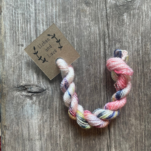 A skein of Marsh Lily variegated embroidery yarn labelled 'Lichen and Lace'.