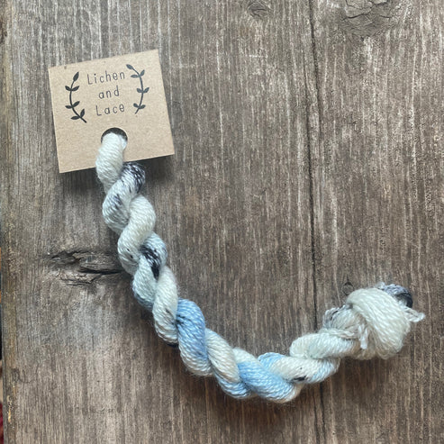 A skein of Rainy Day blue and white embroidery yarn labelled 'Lichen and Lace'.