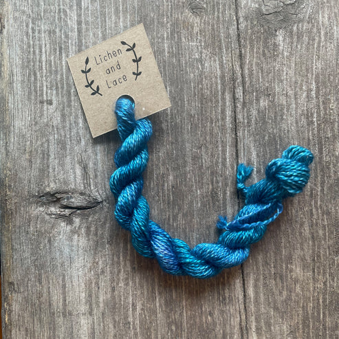 A skein of Teal Tide blue embroidery yarn labelled 'Lichen and Lace'.