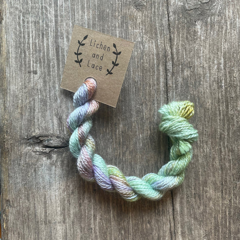 A skein of Wild Flowers pastel variegated embroidery yarn labelled 'Lichen and Lace'.