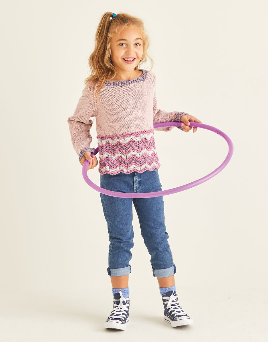 Young girl wearing a sweater with a chevron detail at the bottom hem,  holding a purple hula hoop against a plain background