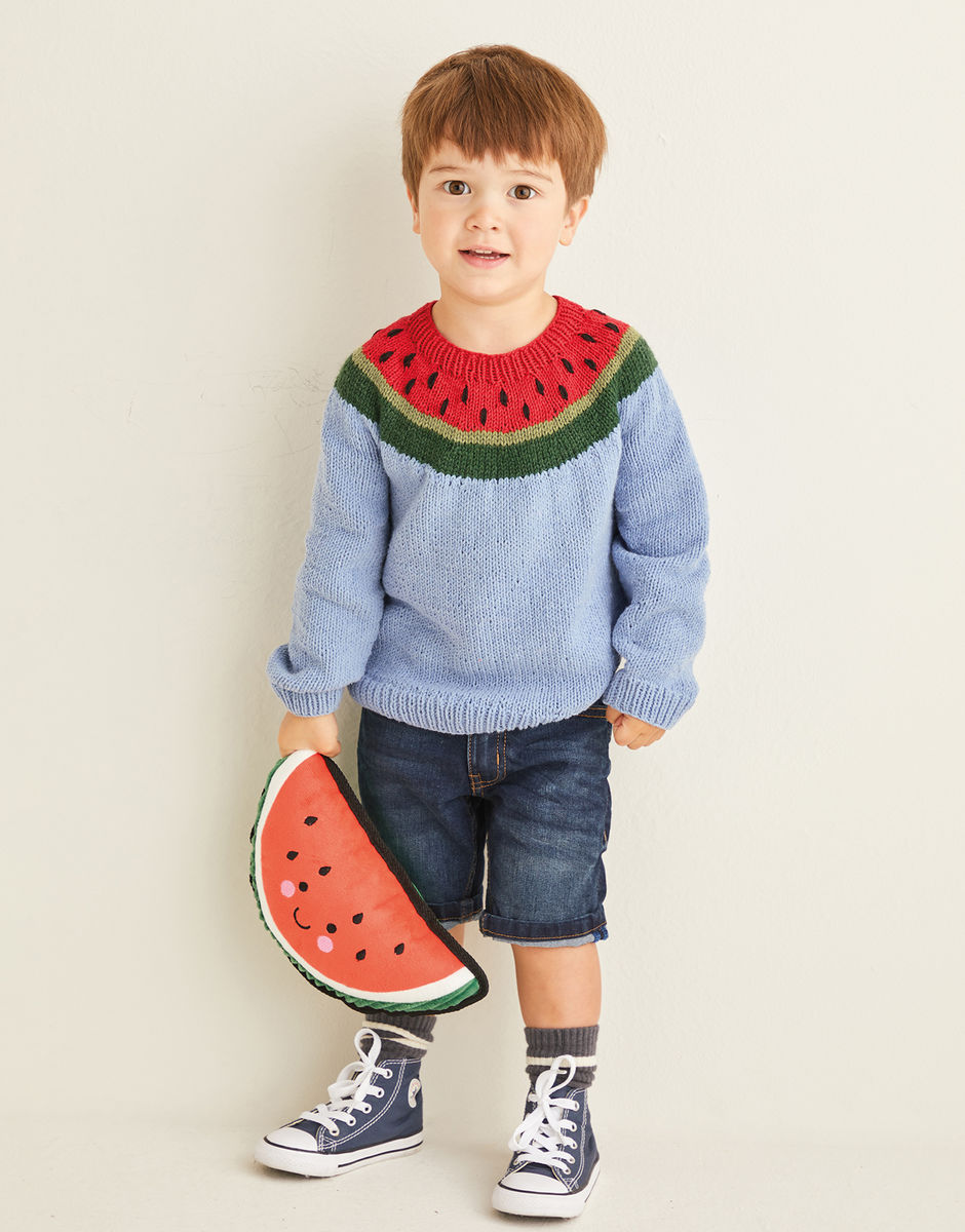 Child wearing a blue sweater with watermelon design, holding a watermelon-shaped pillow against a beige background