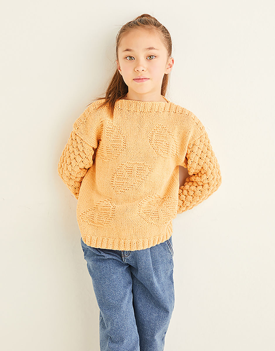 Young girl wearing a pale orange sweater with orange segment motifs and blue jeans against a plain background