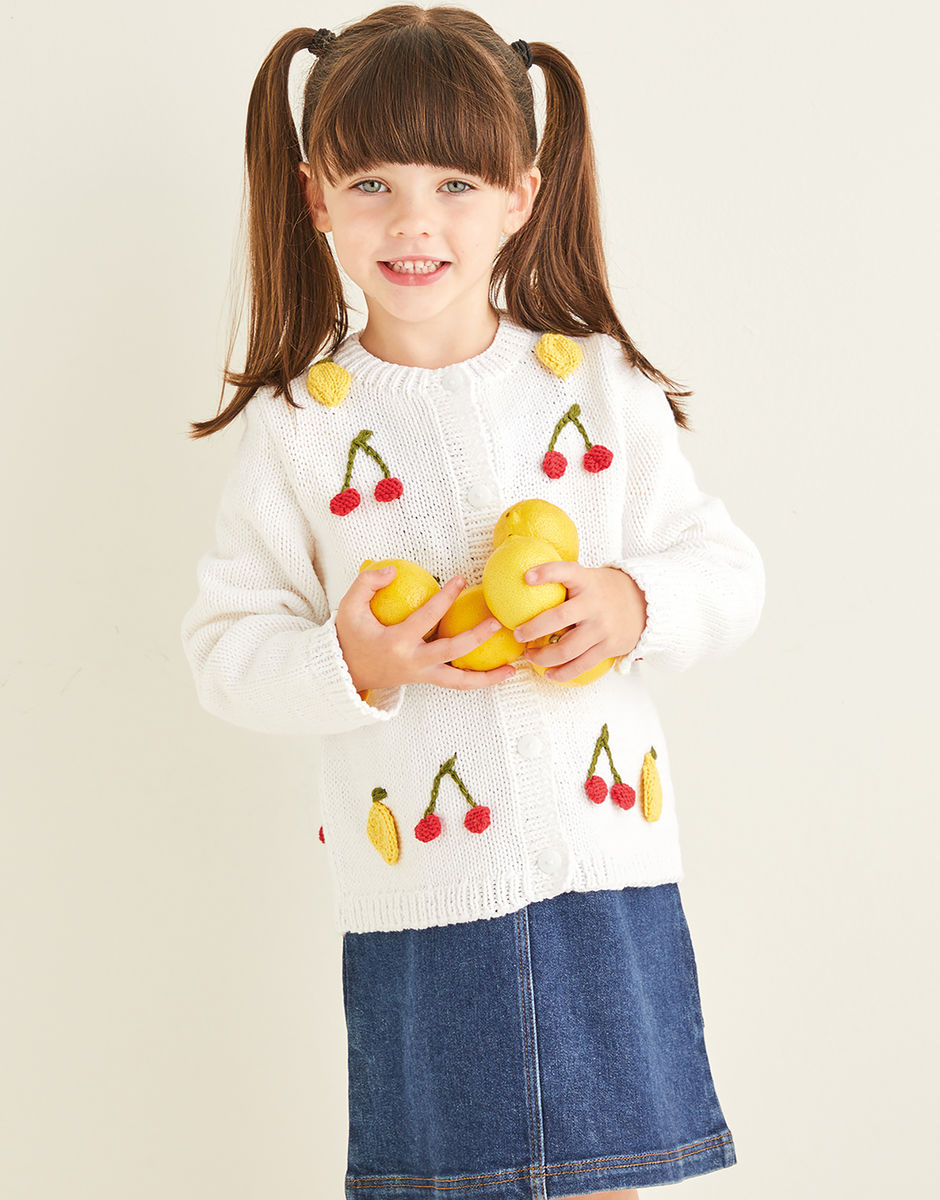 Child wearing a sweater with fruit designs holding lemons against a plain background