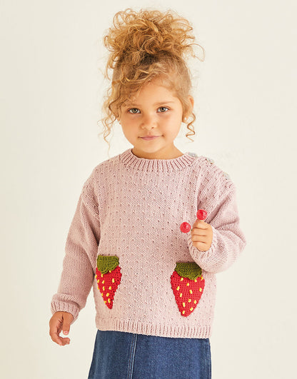 Child wearing a pink sweater with strawberry designs, holding two red objects.