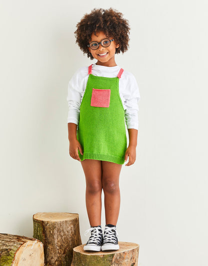 Child wearing a green dress with pink accents standing on wooden logs against a white background