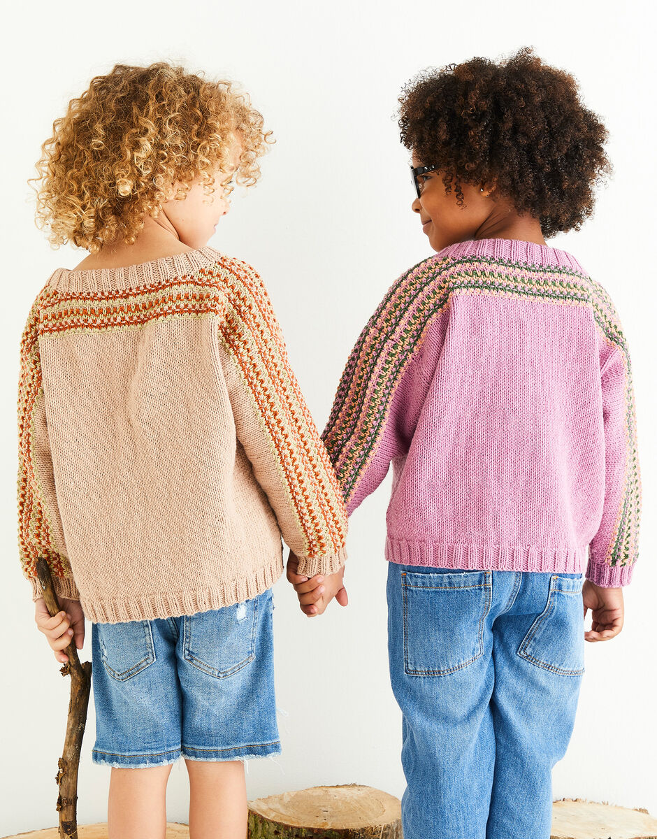 Two children wearing patterned sweaters holding hands against a white background