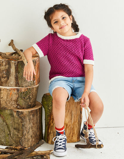 Child wearing a pink knitted sweater and denim shorts sitting on a wooden log.