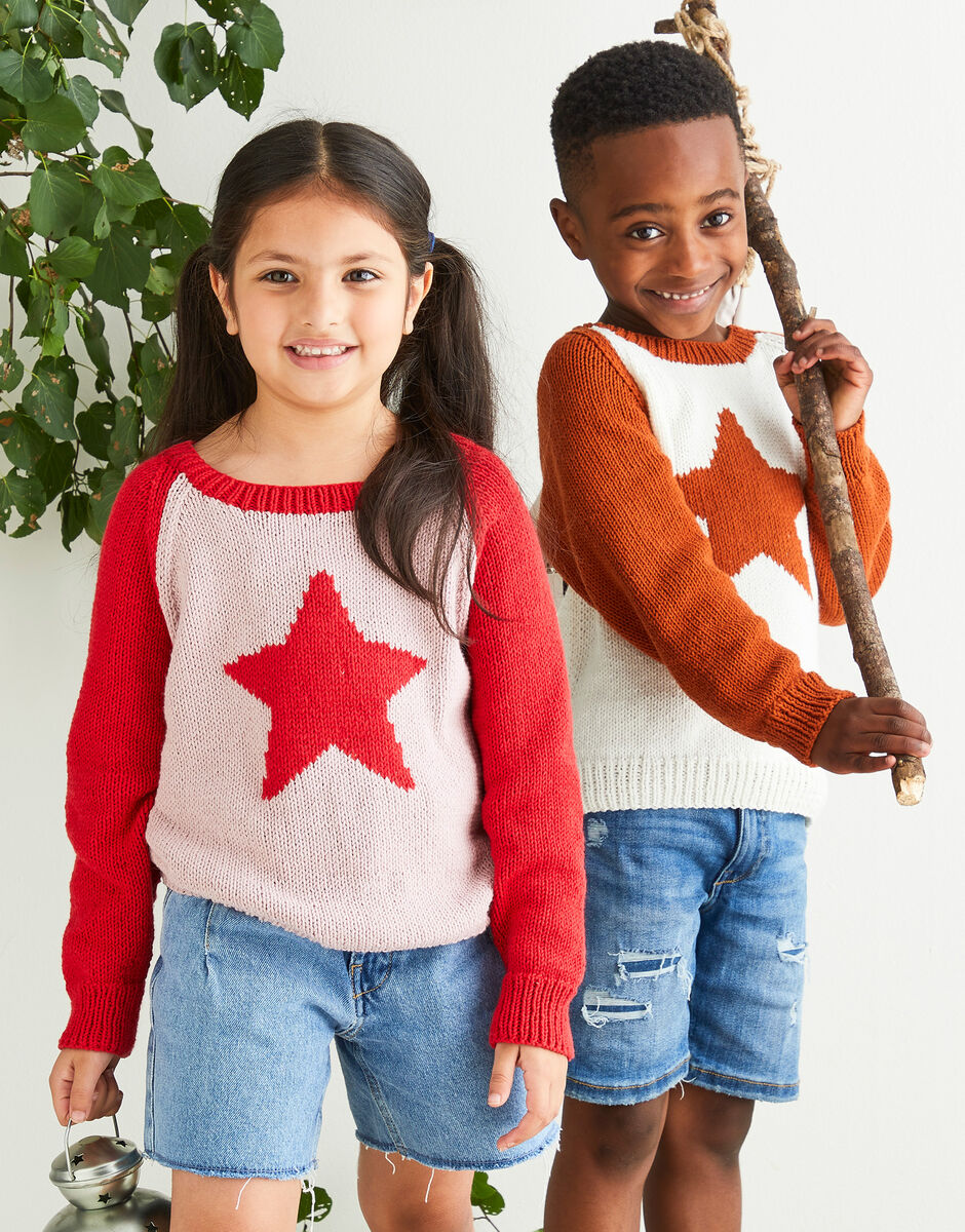 Two children wearing star-patterned sweaters standing outdoors with a plant in the background.