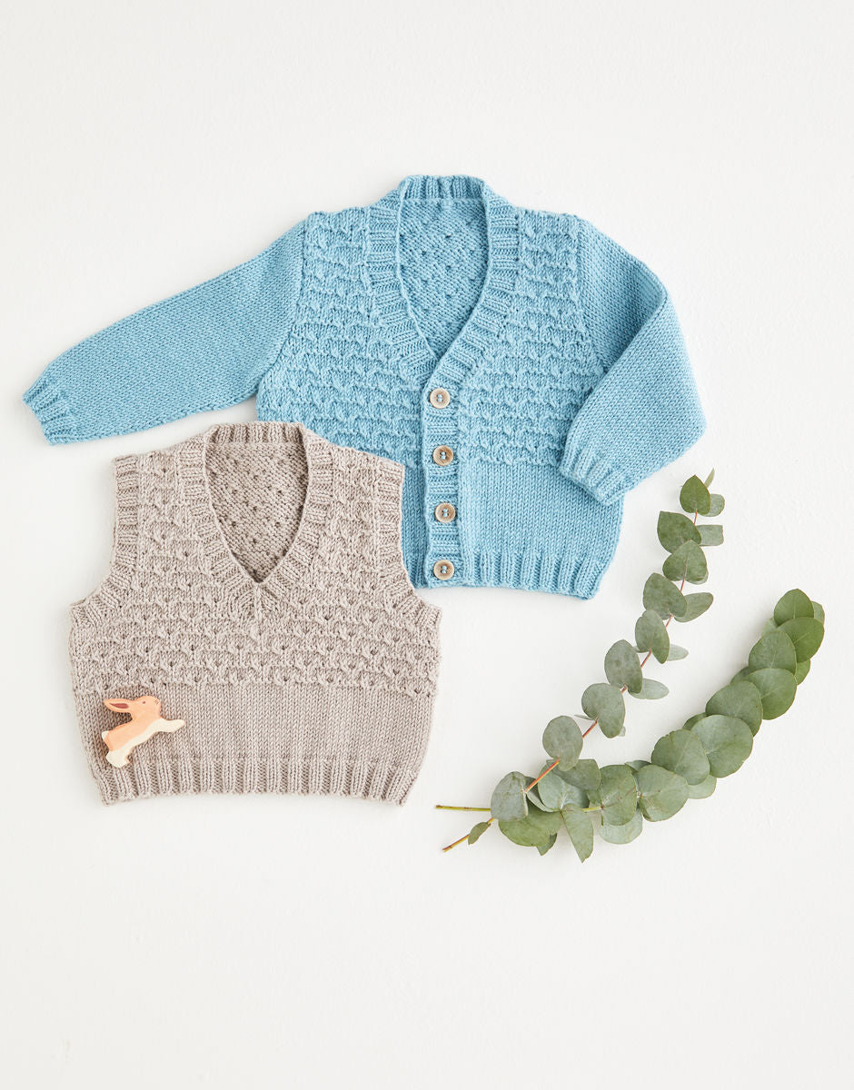 Blue knitted cardigan and gray knitted vest on a white background with greenery.