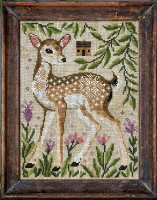 Cross-stitched deer in a natural setting with leaves and flowers, framed in wood.