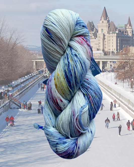 White skein of merino and nylon yarn with colourful flecks in front of a cityscape of Ottawa with people skating on the canal
