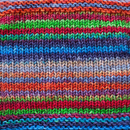 a knitted swatch of merino yarn with blue, green, red, and purple tones from Urth yarns