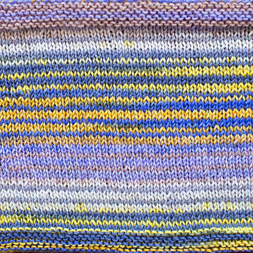 a knitted swatch of merino yarn with yellow, purple, and blue tones from Urth yarns