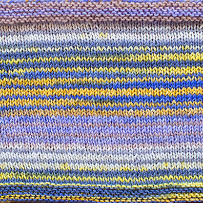 a knitted swatch of merino yarn with yellow, purple, and blue tones from Urth yarns
