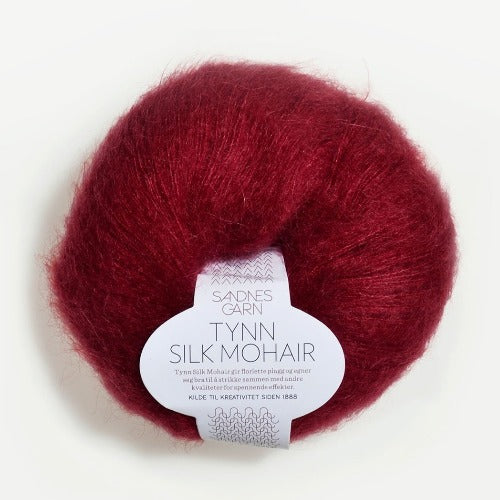 A ball of Tynn Silk Mohair yarn in a deep red color with a 'Tynn Silk Mohair' label from Sandnes Garn