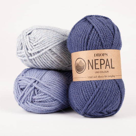 Three skeins of DROPS Nepal yarn in blue, gray, and purple colors, arranged on a flat surface.