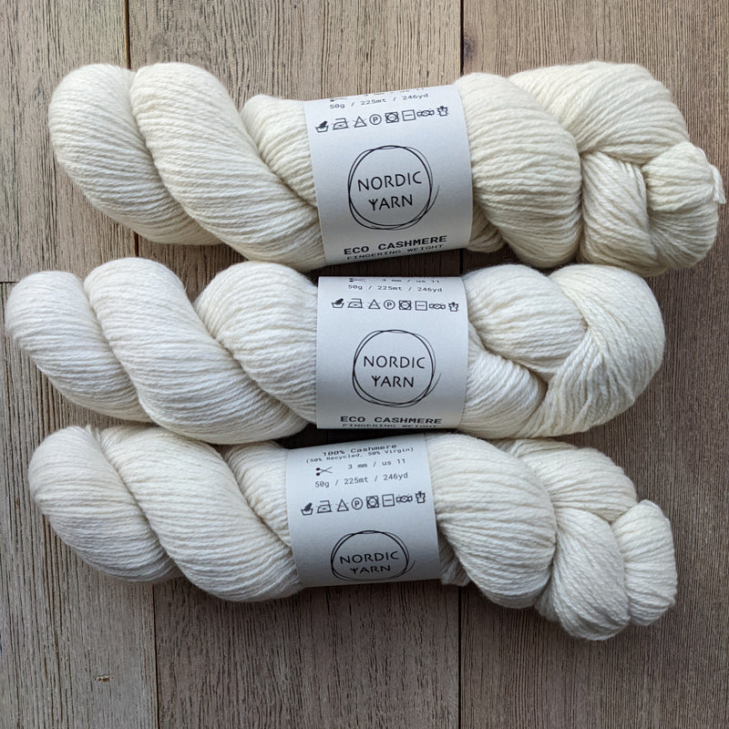 Three skeins of white Eco Cashmere Fingering yarn by Nordic Yarn, displaying the yarn's texture and natural color.
